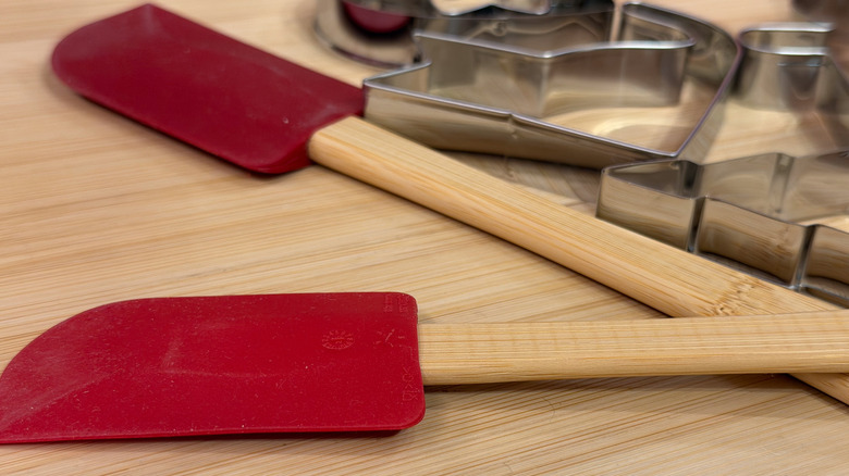 Red silicon spatulas with wood handles on a wood surface with metal cookie cutters