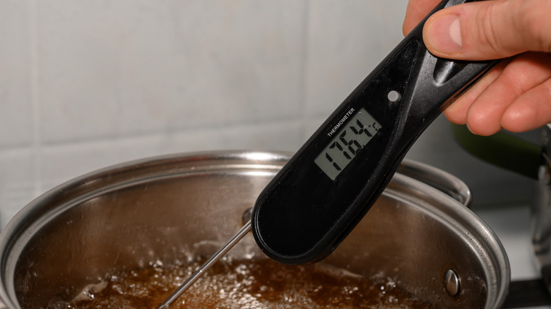 Hand holding a digital thermometer in hot liquid in a pan with the display reading 176.5
