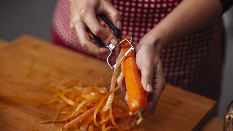 Hands peeling a carrot over a cutting board with a y-shaped vegetable peeler