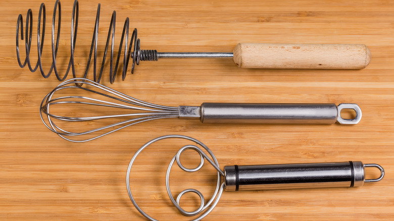 three different kinds of whisks sitting on a wood surface