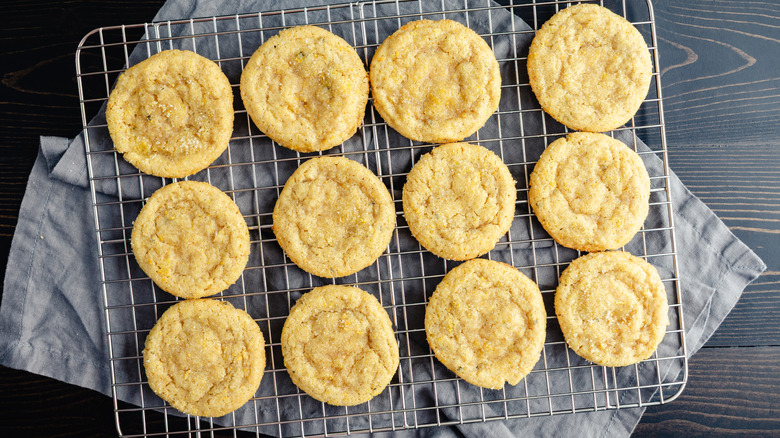 twelve snickerdoodle cookies cooling on a wire rack over a towel on a wood surface