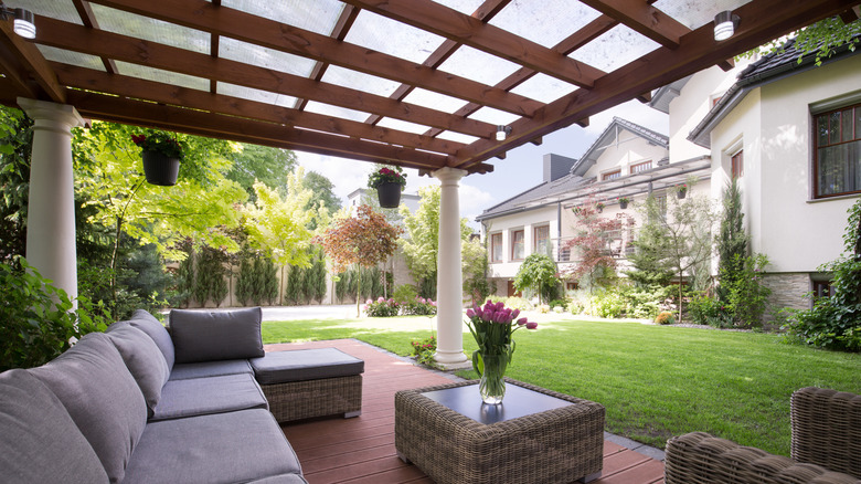 A covered patio with a large sectional and flowers on the center table