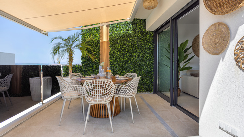 A covered patio with white furniture and round wood table in the middle