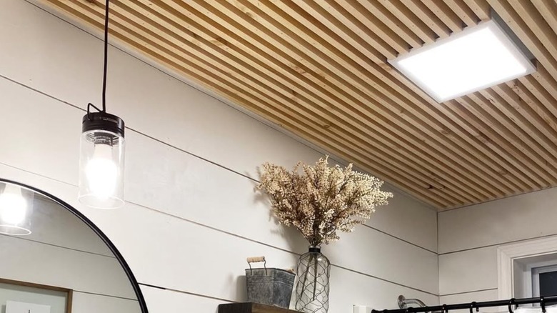 A bathroom ceiling with wood slates and square light.