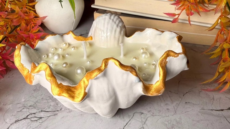 A clamshell candle holder with gold edging and pearls in the wax candle.