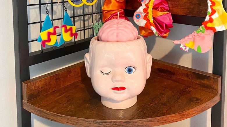 A quirky brain candle in a ceramic doll head holder on a wooden corner table.