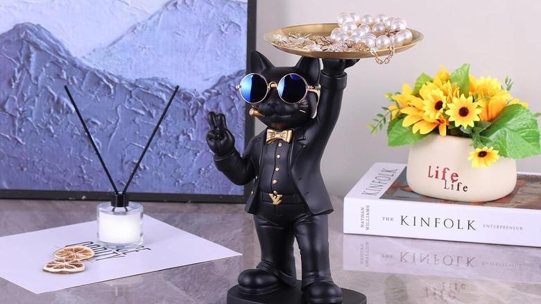 A black and gold butler cat statue holds jewelry on a counter.