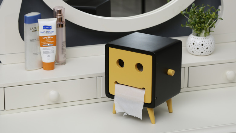 A yellow and black tissue box designed like a TV sits on a bathroom vanity.