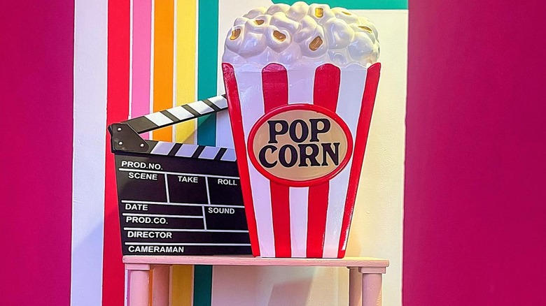 Clapperboard and popcorn decor on a pink table.