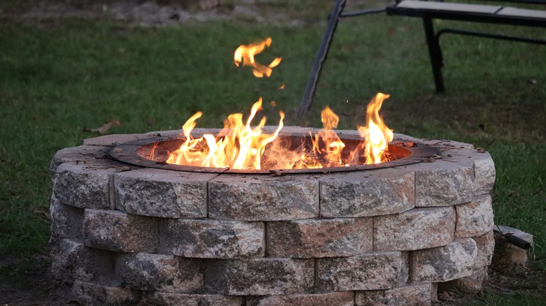 Lit fire pit in a backyard, the flames erupting from a stone base