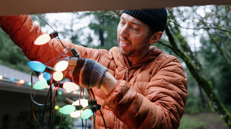 Man stringing up holiday lights in blue, white, and green on home