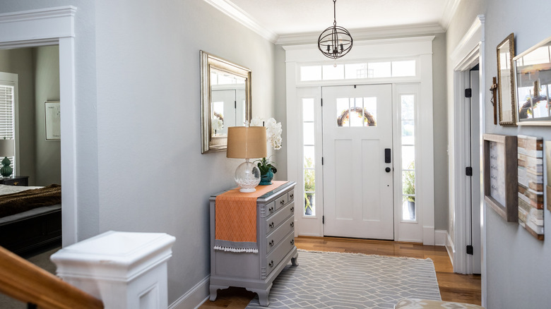 A chest of drawers housing a lamp and flower vase in an entryway