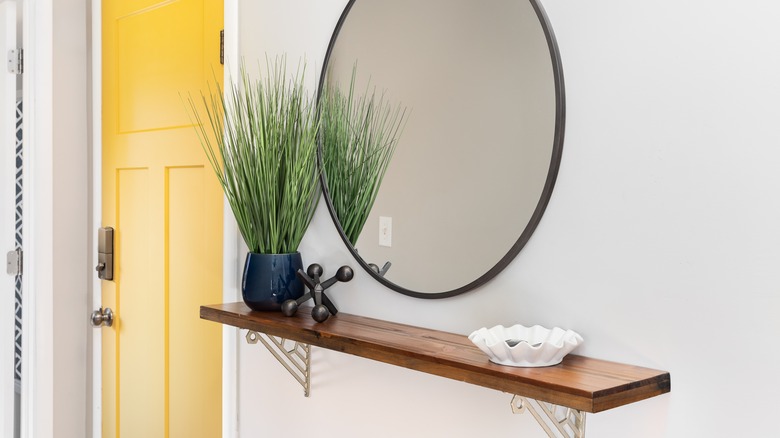 A wood floating shelf with a white holder and vase