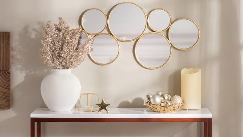 A cluster of mirrors above a white console table holding decor