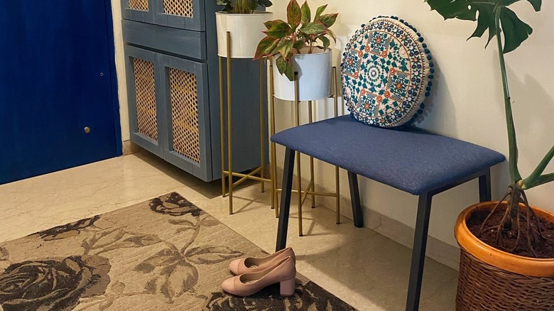 A entryway with floral rug, funky cushion, and plants