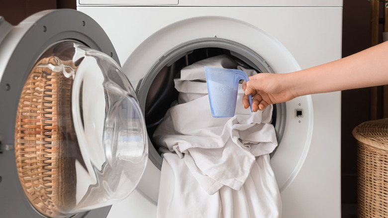 Person washing sheets in washing machine and holding detergent