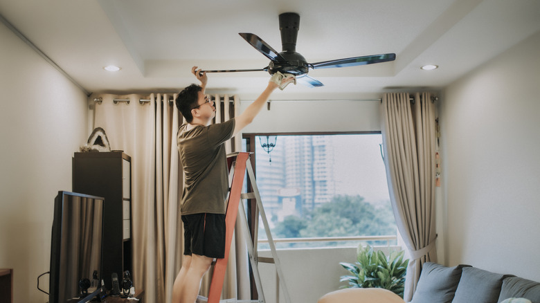 Person cleaning ceiling fan in living area