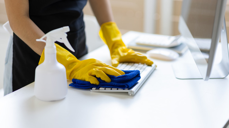 Person cleaning computer keyboard with spray solution and rag