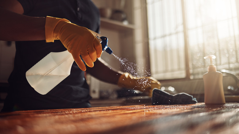 Person cleaning countertop with rag and spray solution