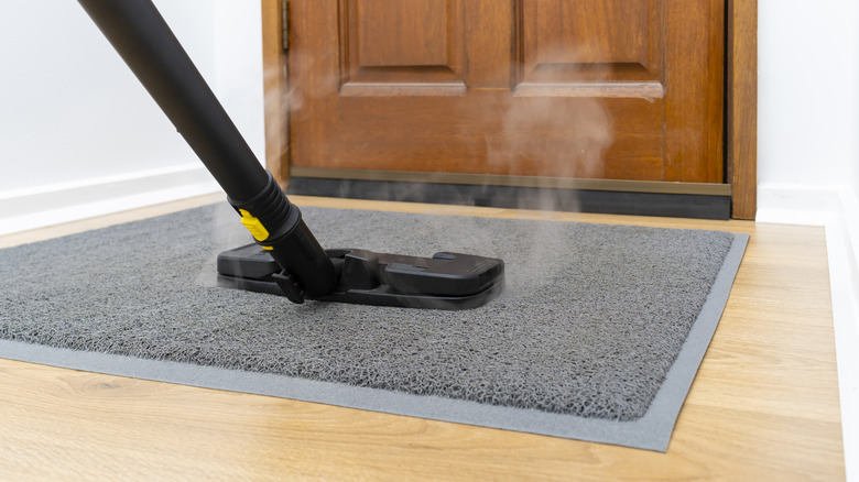 Person steam cleaning doormat