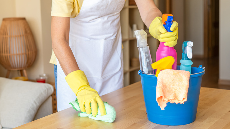 Person reaching into bucket with cleaning supplies while wiping countertop