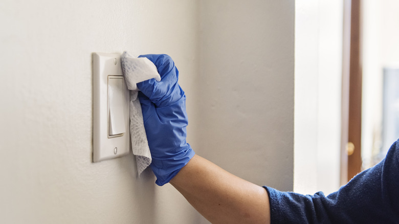 Person cleaning light switch while wearing gloves