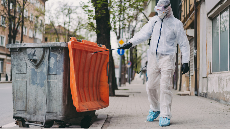 Person wearing PPE washing trash can outside