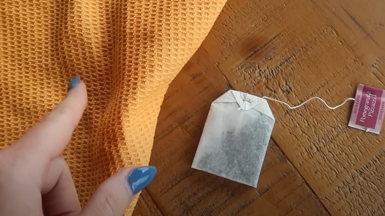 Someone pointing at a microfiber cloth and black tea sachet on wood surface