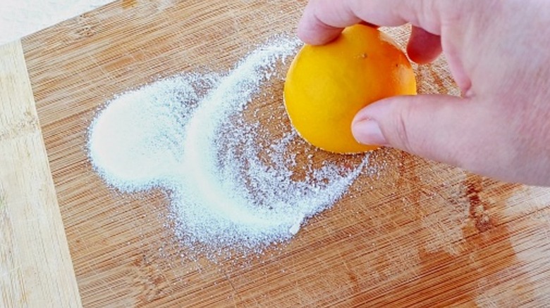 Someone rubbing salt and lemon on wood surface.