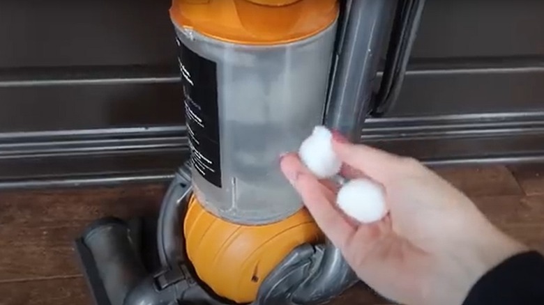 Someone holding cotton balls in front of a vacuum cleaner