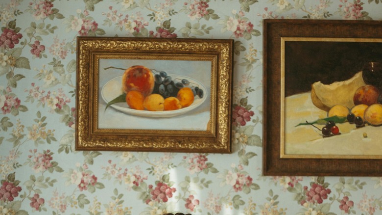 Two paintings hanged on floral wallpaper.