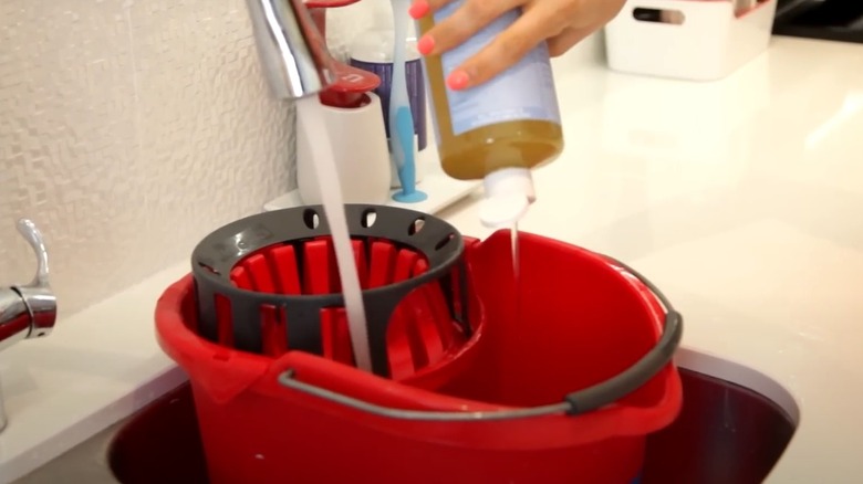 Someone adding Castile soap and water to mop bucket.