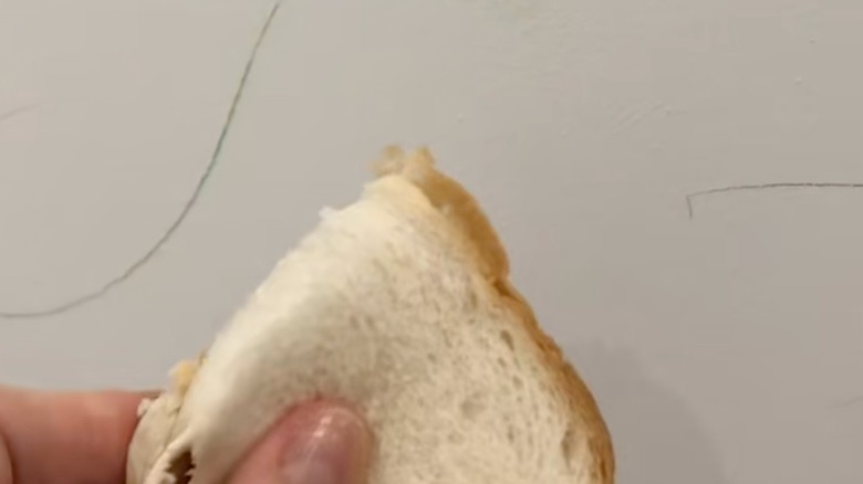 Someone holding bread against wall with pencil marks.
