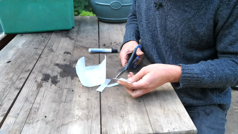 a man cuts up a plastic container to make labels for seedlings