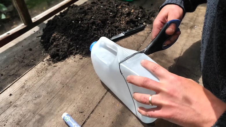 a person cuts a recycled jug to make a plastic scoop