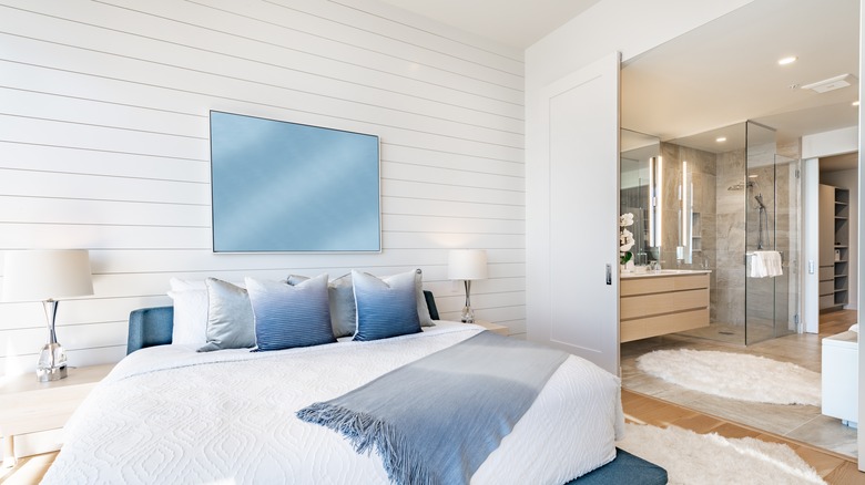 white shiplap accent wall behind white and blue bed next to bathroom