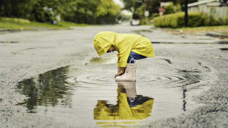 A kid splashing in a puddle with a yellow raincoat