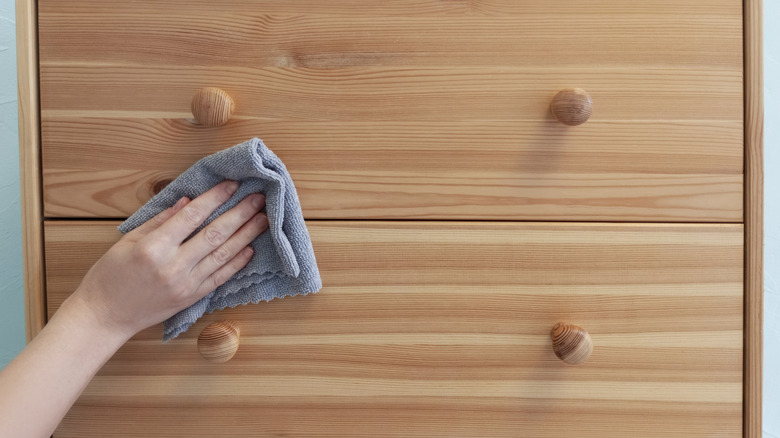 Someone's hand wiping wooden furniture with a cloth