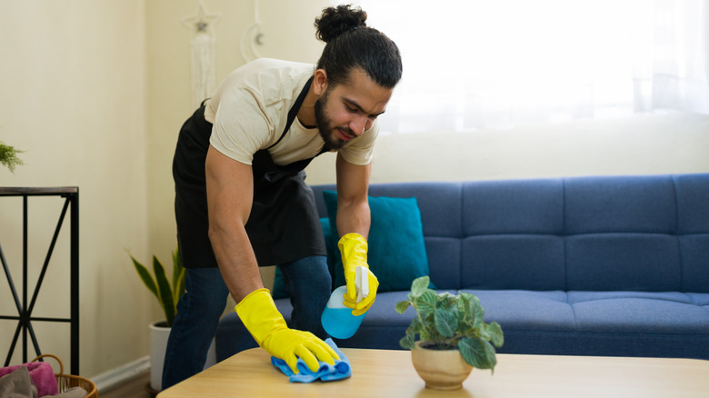 A man dusting table with spray bottle and rag