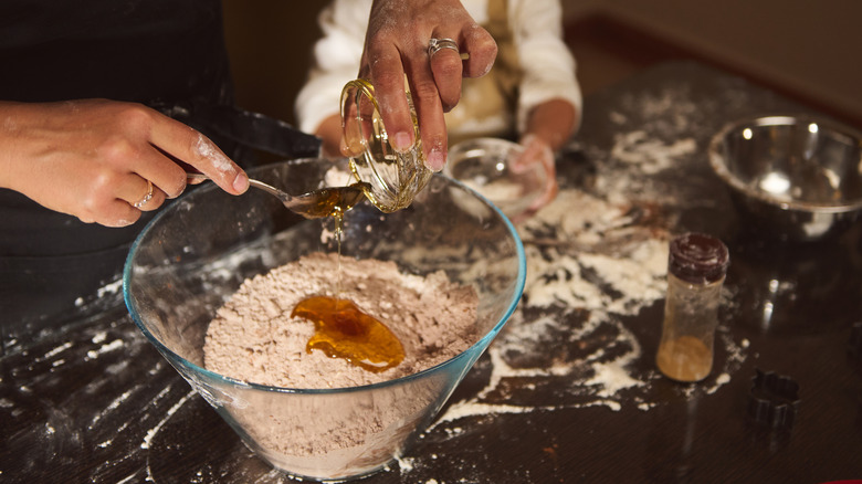 Someone adding honey to a bowl of cocoa and flour