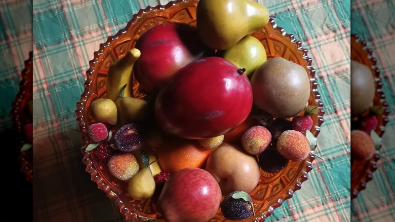 orange glass bowl with fake fruit inside on plaid tablecloth