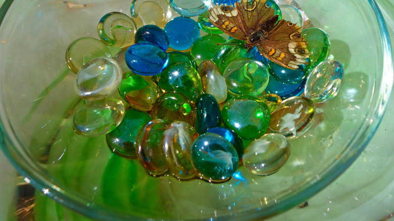 glass bowl with blue, green, brown, and white glass stones and a moth