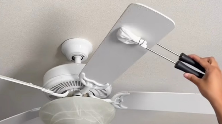 Someone using tongs and a coffee filter to dust fan.