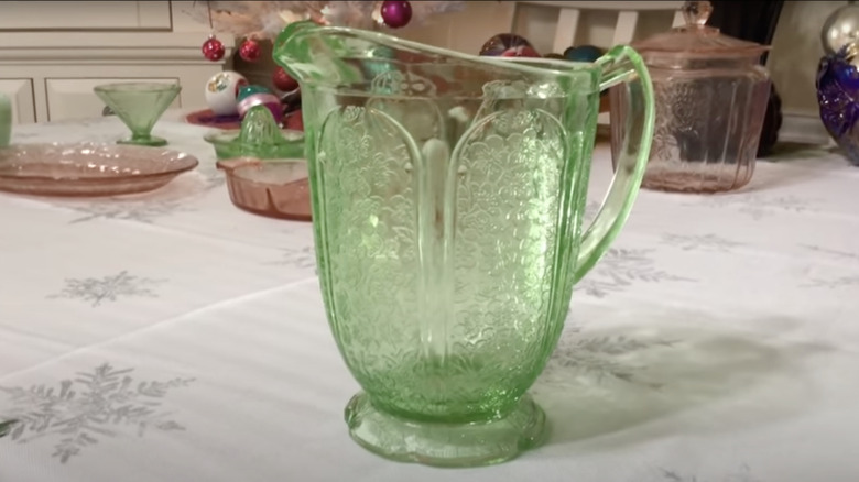 A green pitcher in the Cherry Blossom pattern by Jeannette Glass Company sits on a tabletop.
