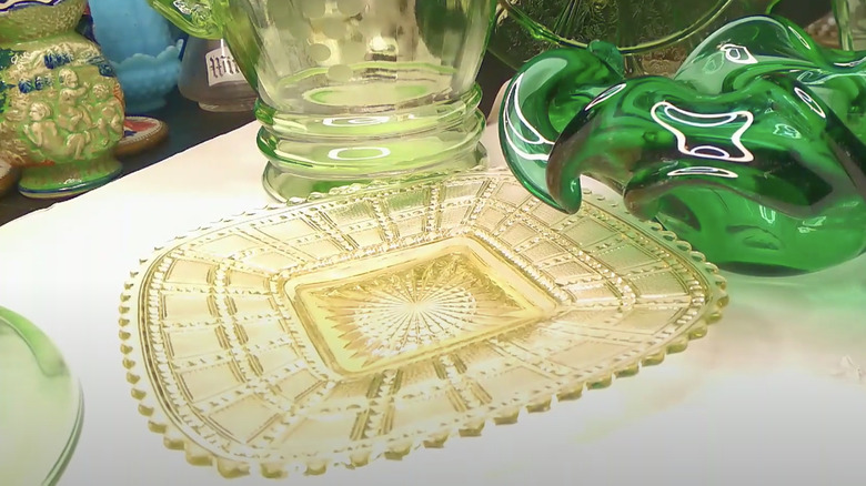 A Depression glass plate in the Beaded Block pattern by Imperial Glass Company sits on a white shelf