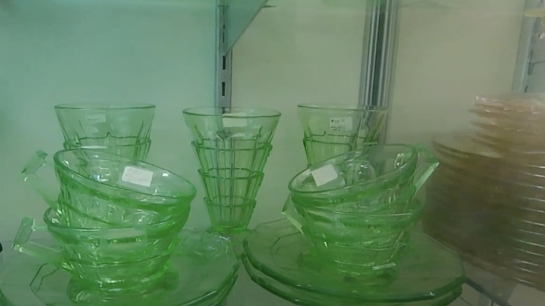 A set of green Tea Room patterned cups and saucers by Indiana Glass Company sit in a cabinet at a thrift store.