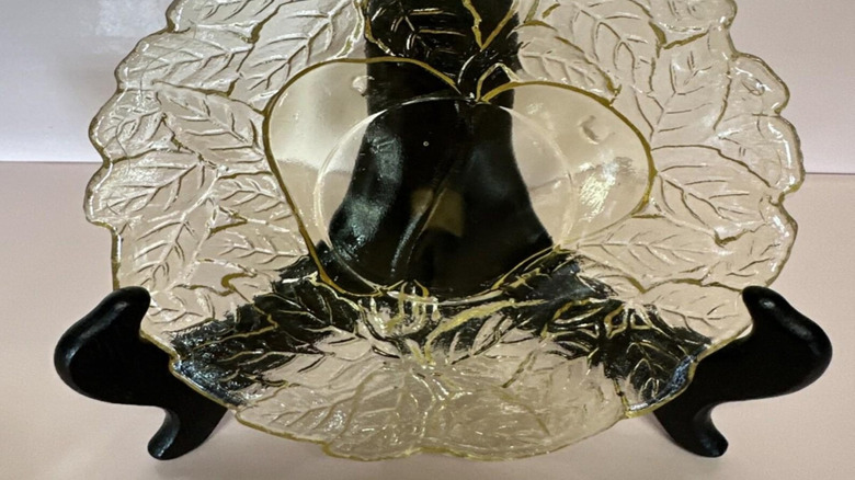 An amber plate with the pattern Avocado or Sweet Pear by Indiana Glass Company sits on a black display stand.