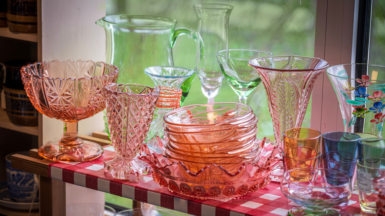 A shelf with a checkered tablecloth is covered in colorful depression glass dishes, cups, and vases.