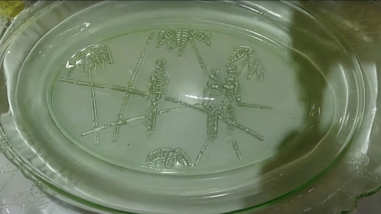 A green serving platter adorned with parrots by the Federal Glass Company on display in a thrift store.
