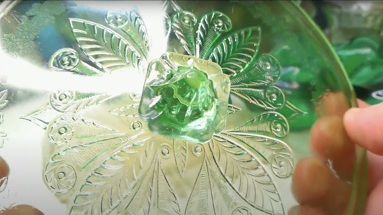 A collector holds a green glass lid featuring the Adam pattern by Jeannette Glass Company